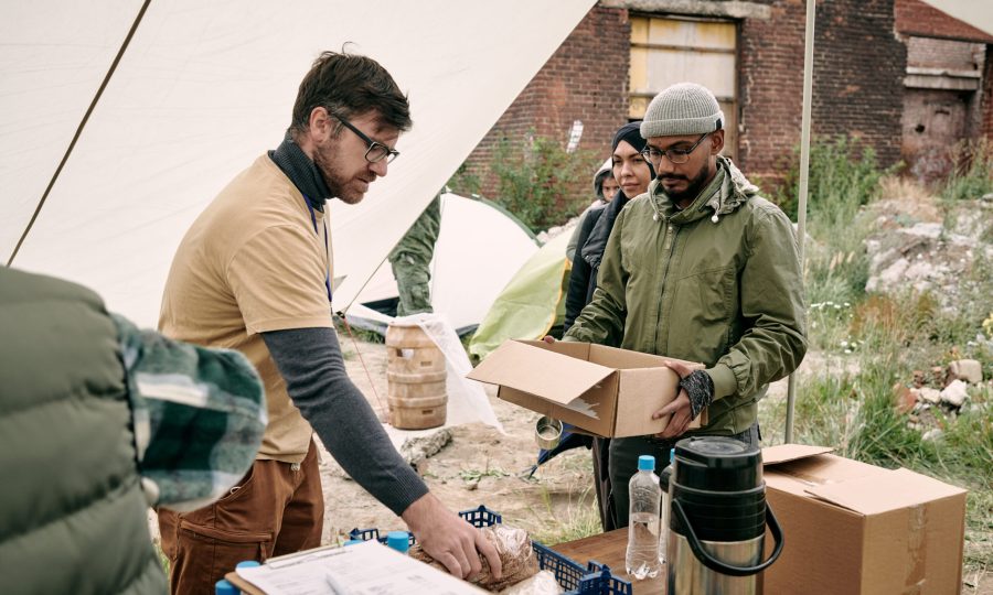 Bearded volunteer in yellow tshirt standing in food tent and giving food to refugees